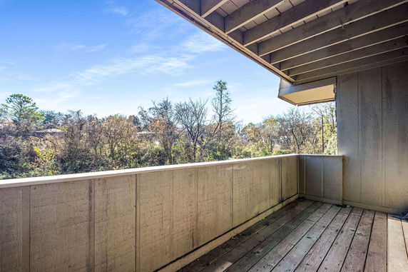 Wooden balcony with railing overlooking trees and sky.