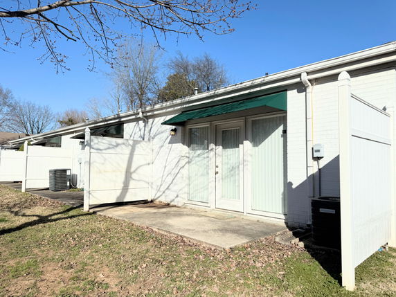 Front view of a single-story house with a green awning over the door and white fencing.
