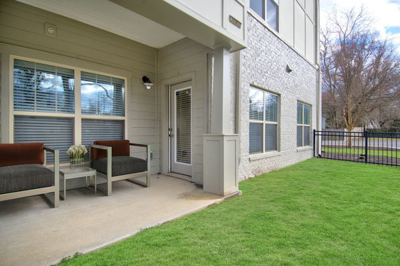 Outdoor view of a building's side entrance with two chairs and a small table on a patio.