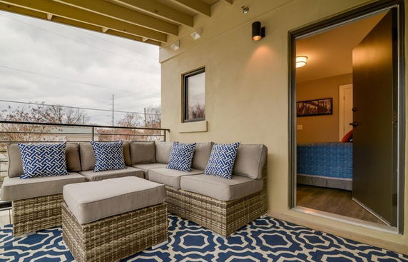 Outdoor seating area attached to a house with a view of surrounding trees and sky.